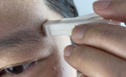 A small white plastic device being held to a man's forehead